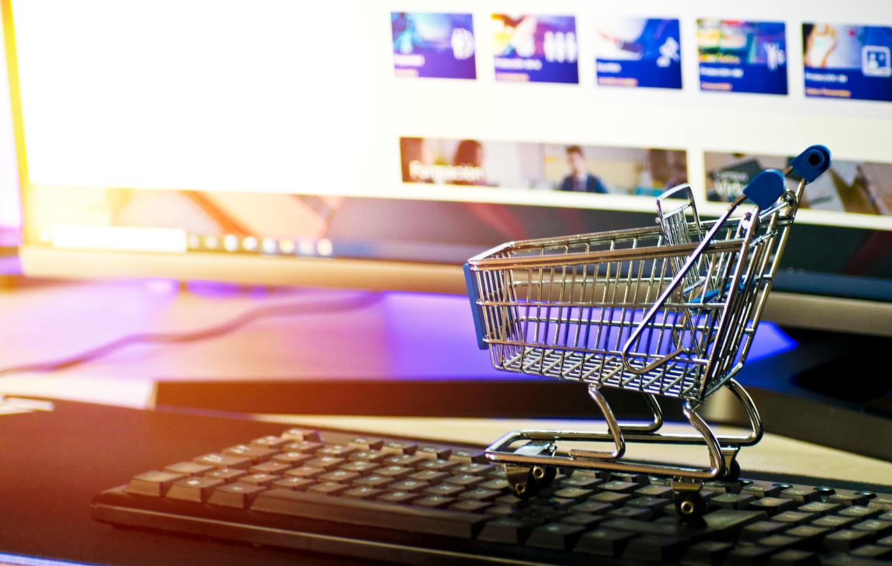 Mały wózek sklepowy stojący na klawiaturze komputera symbolizujący zakupy internetowe